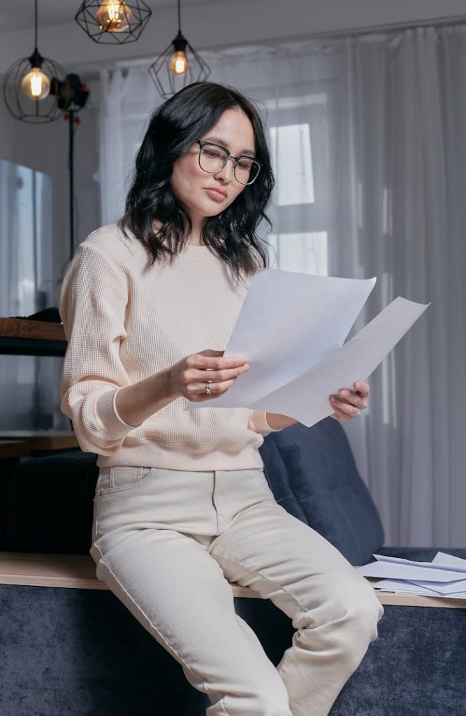 Thoughtful woman analyzing papers while seated indoors, reflecting on finance or work.